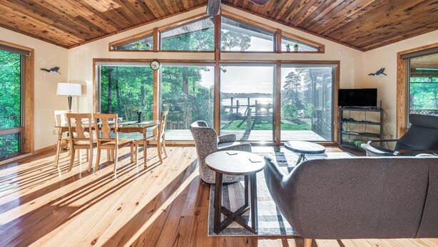 A spacious room with wooden flooring, large windows, a ceiling fan, and a dining area with chairs and a table. - Waterfront Lancaster Cabin ~ 10 Mi to Kilmarnock! (Lancaster)