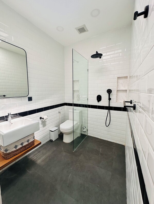 A modern bathroom with white subway tiles, a glass-enclosed shower, a white sink, and a toilet. - Beach Bliss: 4-Bed Villa Melodia, Canggu (Berawa)
