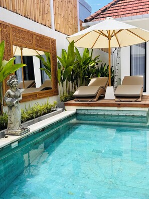 A pool area with two lounge chairs, a statue, and a large umbrella. - Beach Bliss: 4-Bed Villa Melodia, Canggu (Berawa)
