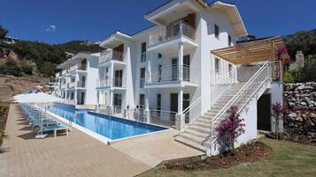 A modern multi-story hotel with a swimming pool, outdoor seating, and a stone wall.