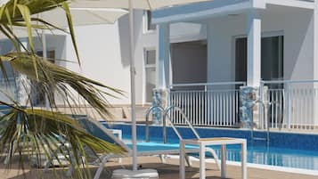 A pool area with lounge chairs, a palm tree, and a covered seating area.