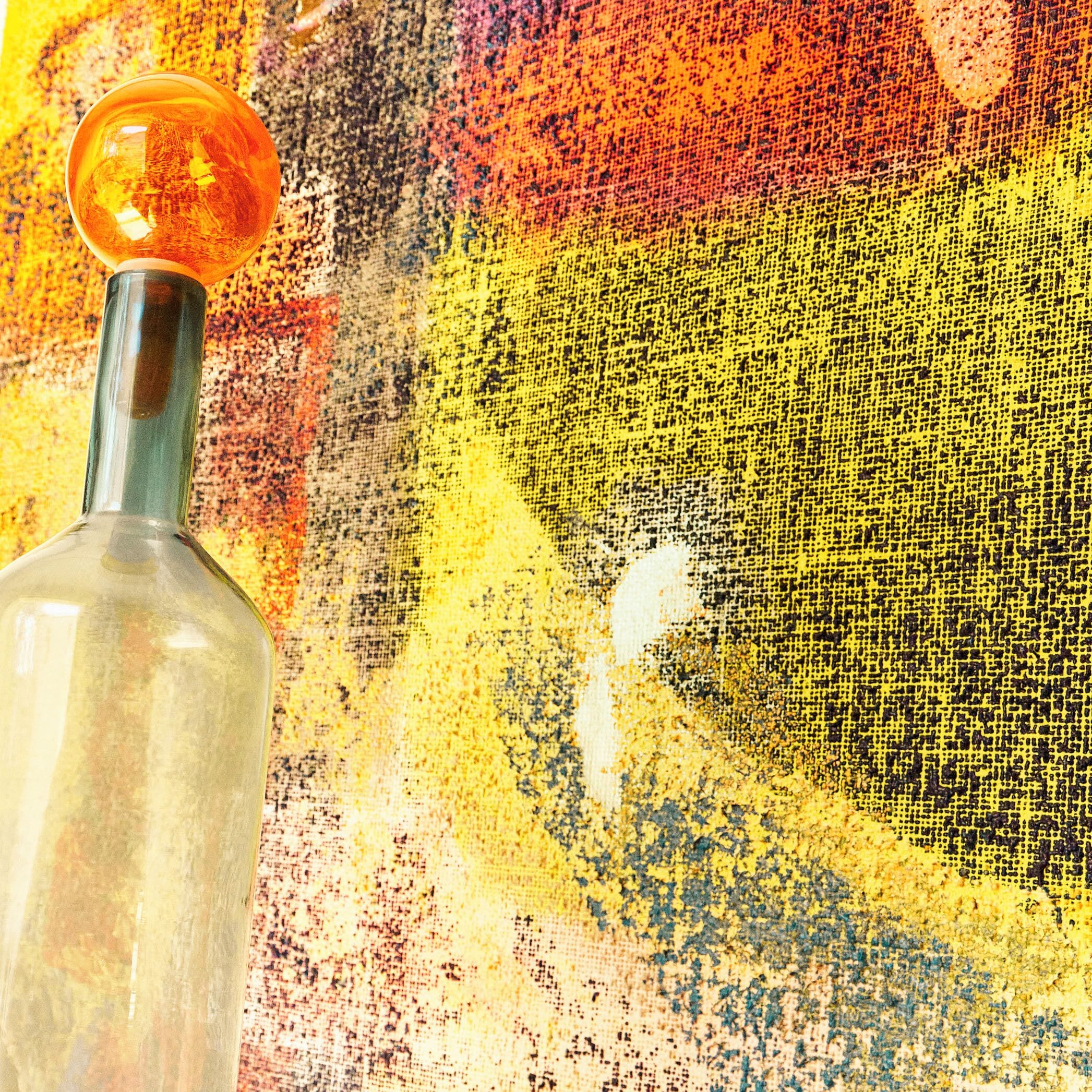 Une bouteille en verre transparent, dotée d’un bouchon arrondi, placée sur un fond texturé.