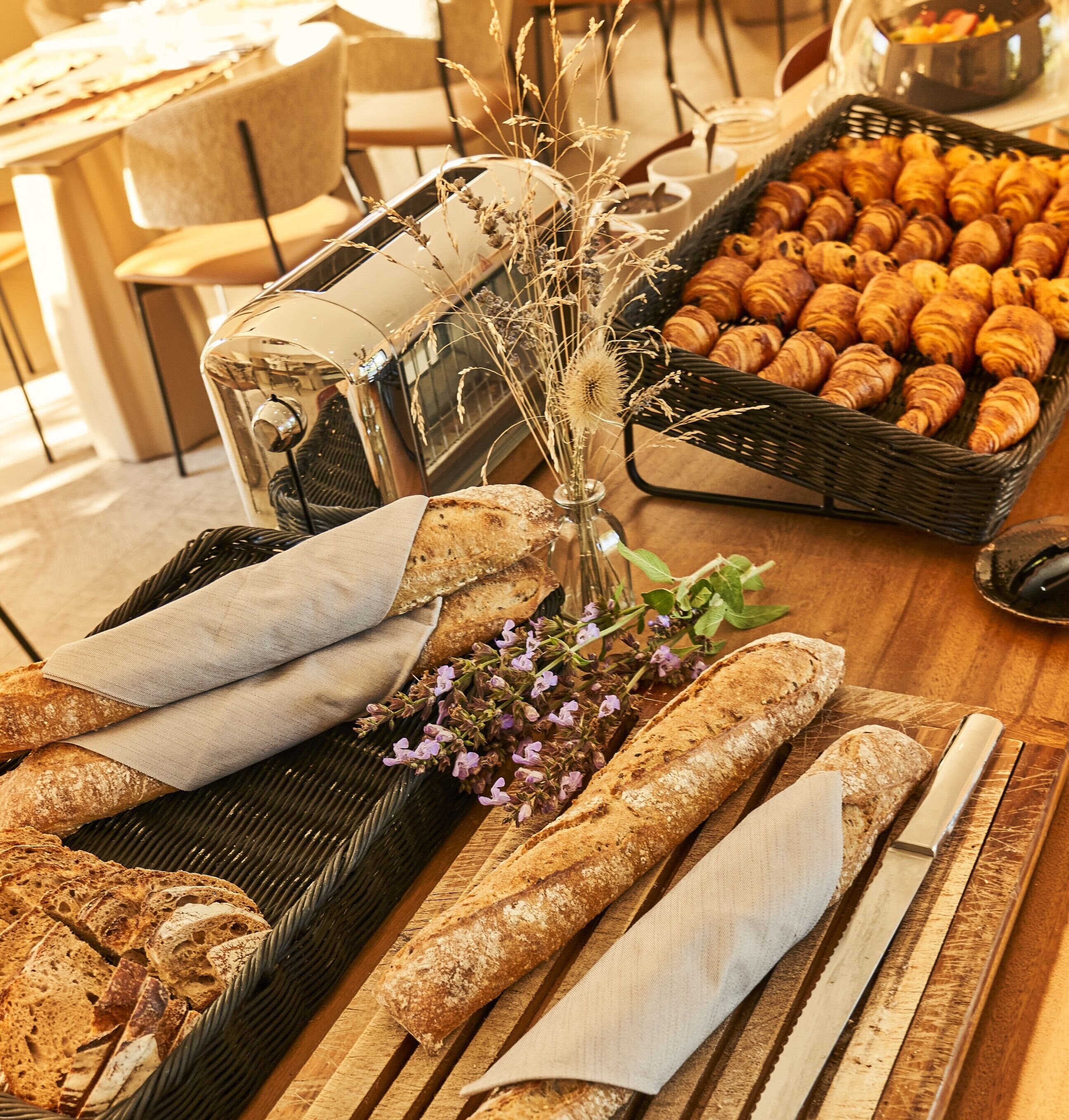 A table with bread, croissants, and a vase with dried plants.