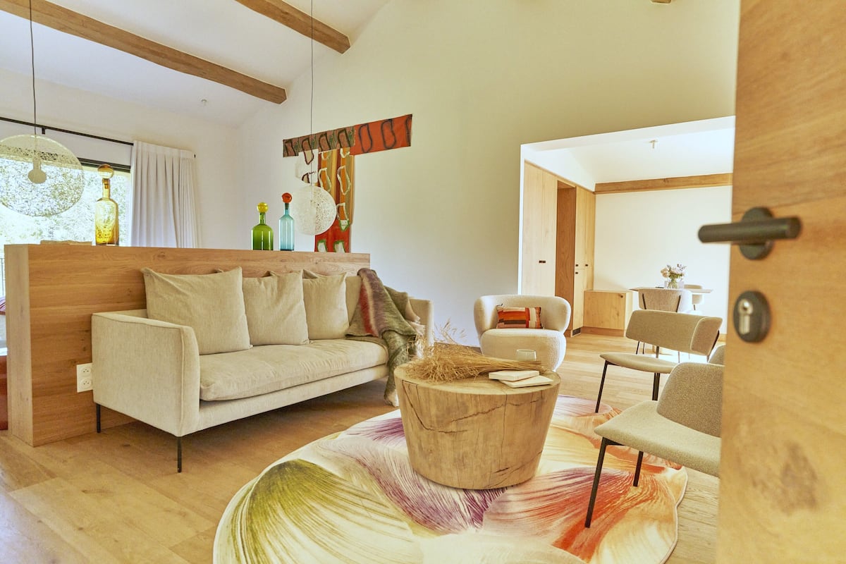 A modern living room with a wooden sofa, a round coffee table, and a colorful rug.