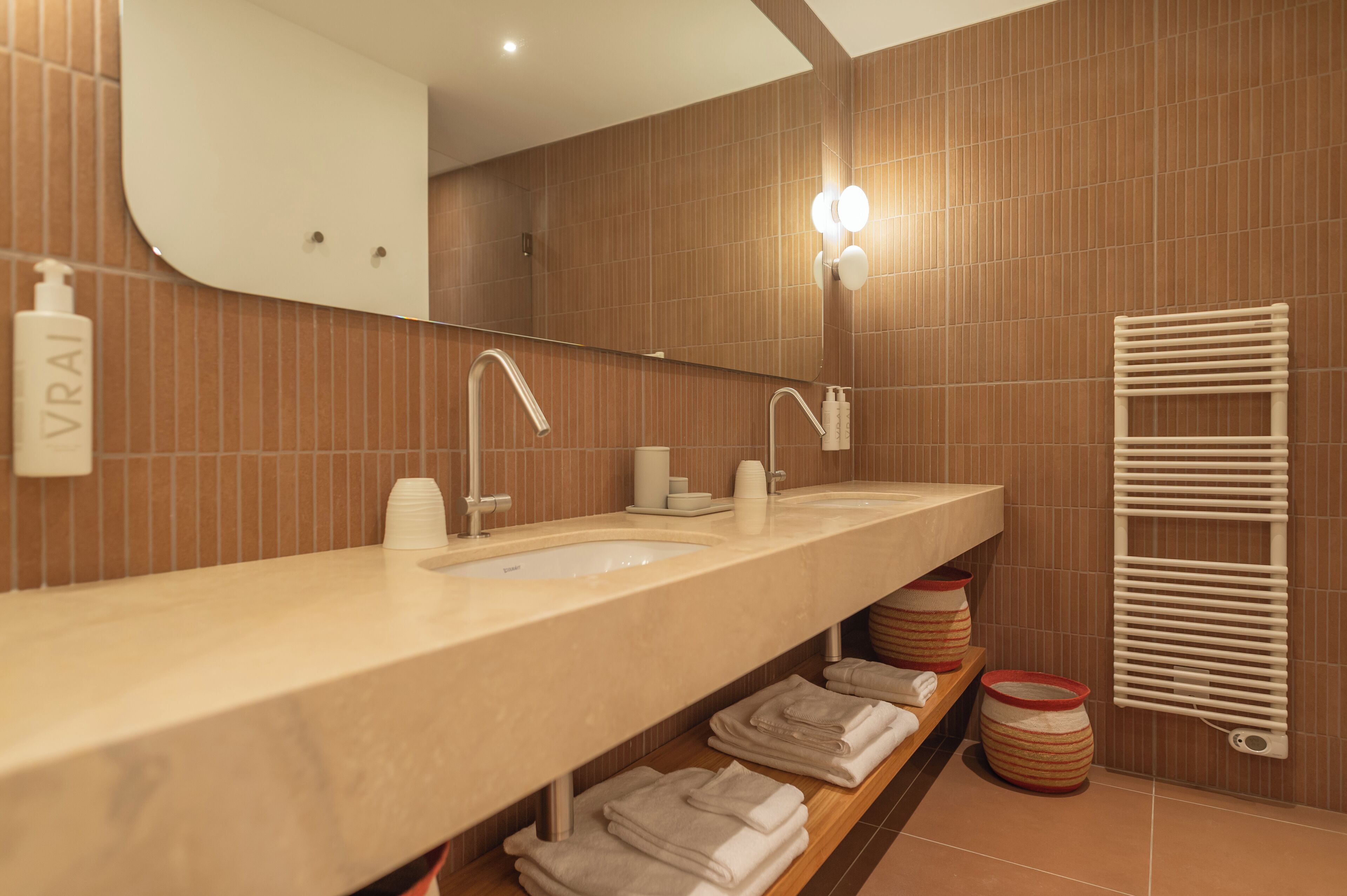 Une salle de bain moderne avec un meuble-lavabo à deux vasques, un grand miroir, un porte-serviettes et une bouteille de shampoing.