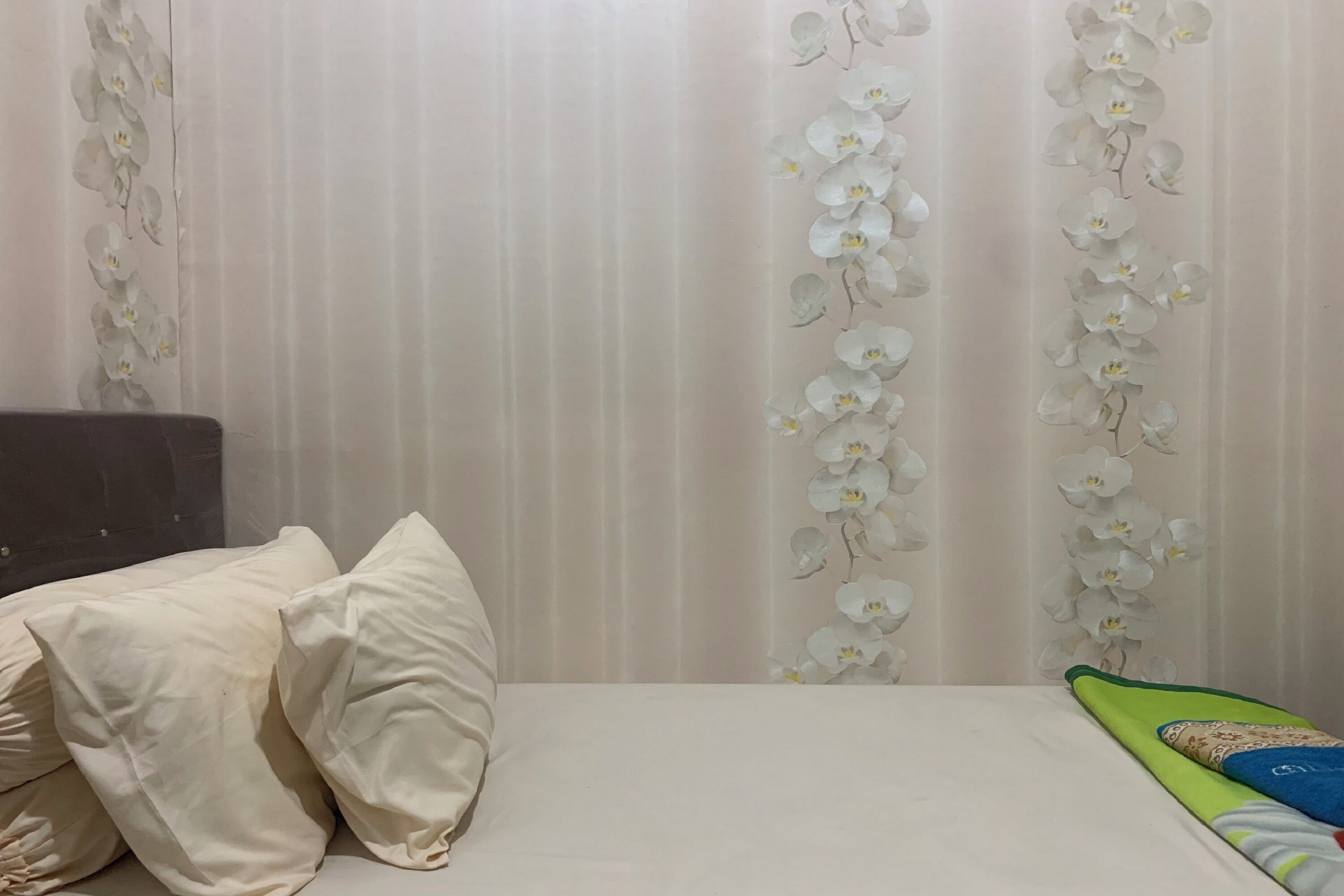 A bedroom with a bed, pillows, and a curtain with white orchid patterns.