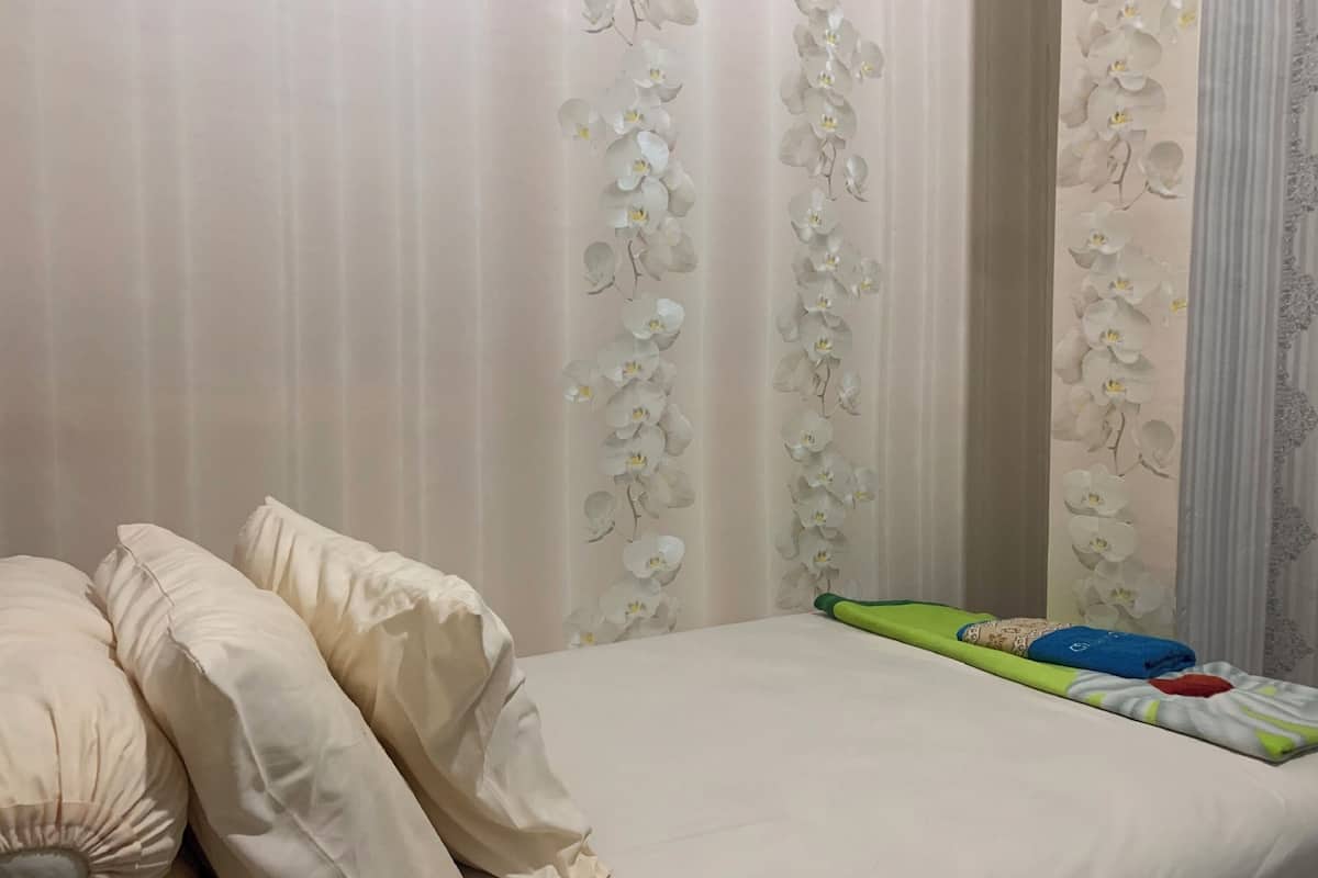 Un dormitori amb un llit, almoines i una cortina amb un dibuix d'orquídees.