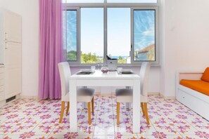 A dining area with a table set for two, a window with a view, and a sofa with an orange cushion. - Bed & breakfast in sorrento with pool and spa (Sorrento)