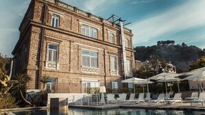 A poolside area with lounge chairs and umbrellas, a brick building with decorative window frames, and a mountainous backdrop. - Bed & breakfast in sorrento with pool and spa (Sorrento)