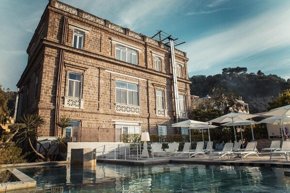A poolside area with lounge chairs and umbrellas, a brick building with decorative window frames, and a mountainous backdrop. - Bed & breakfast in sorrento with pool and spa (Sorrento)