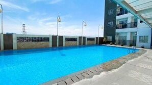 A swimming pool with clear blue water, surrounded by a low wall and a covered area with a glass roof. - OYO 93940 Apartemen Mekarwangi Square By Lina (Bandung)