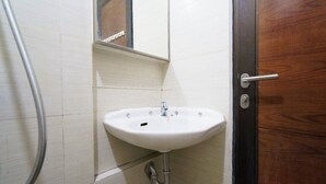 A bathroom with a white sink, a mirror above it, and a wooden door. - OYO 93940 Apartemen Mekarwangi Square By Lina (Bandung)