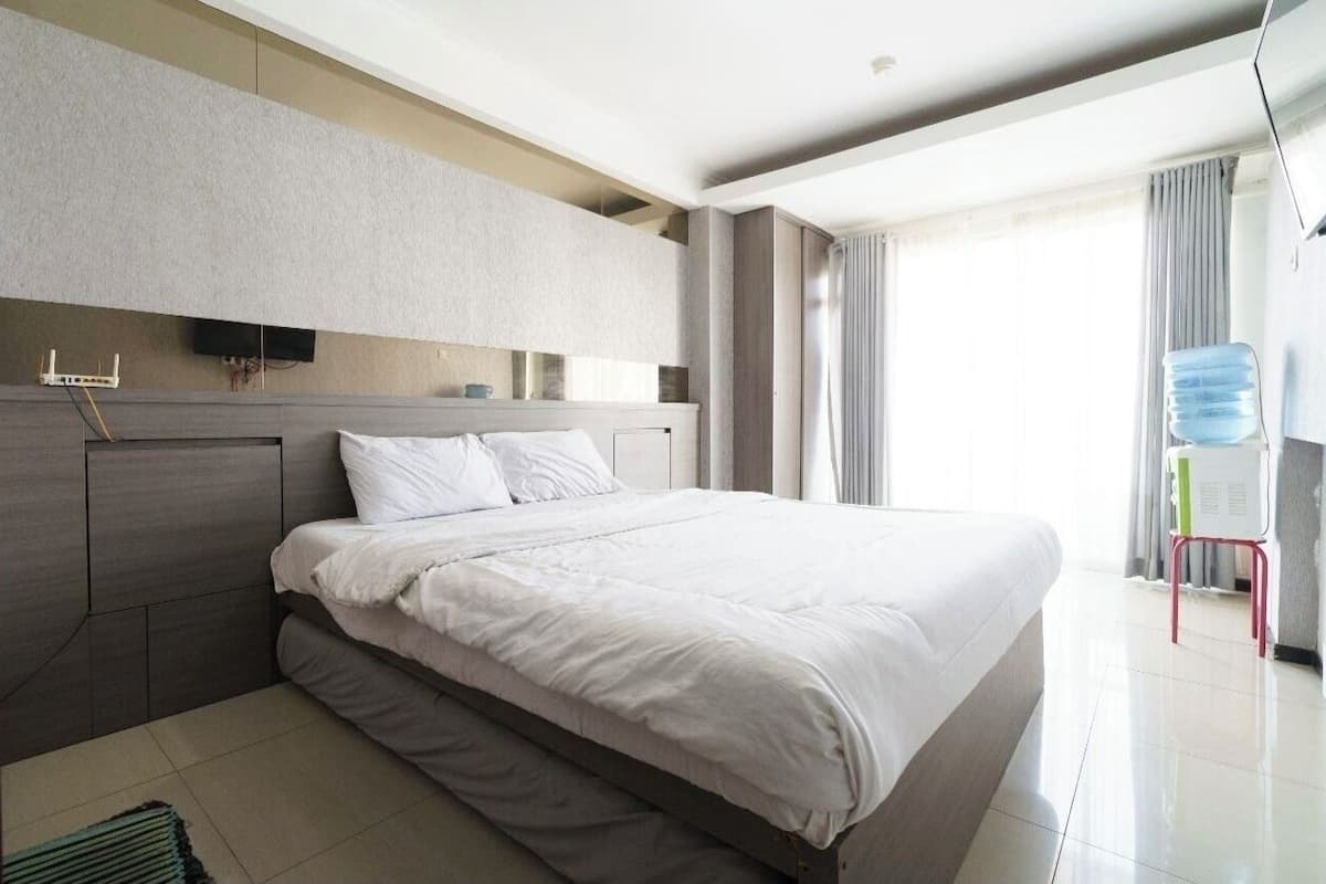 Ein modernes Hotelzimmer mit einem großen Bett, einem flachbildfernseher an der Wand und einem Fenster mit Vorhängen.
