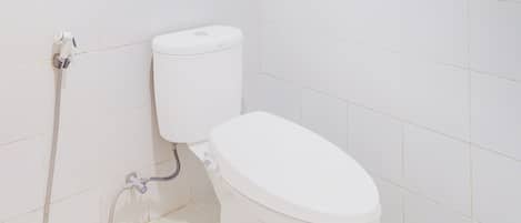 Un baño pequeño y blanco con inodoro, manguera de ducha y un dispensador de papel higiénico en la pared.