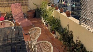 Une terrasse sur le toit offrant une vue sur la ville, aménagée avec une table, des chaises, des plantes en pot et une clôture décorative.