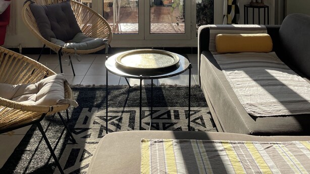 Un salon comprenant un canapé, un fauteuil, une petite table et donnant sur un espace extérieur, visible à travers de grandes portes vitrées, cet espace étant agrémenté de plantes et délimité par une clôture.