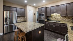 A modern kitchen with stainless steel appliances, dark wood cabinets, granite countertops, and a central island with stools. - NEW Southern Charm ATL 4 Bdr/3 Bath Executive Home (Norcross)