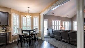 A modern kitchen with dark wood flooring, a dining area with a glass table and chairs, and a living area with a dark leather couch. - NEW Southern Charm ATL 4 Bdr/3 Bath Executive Home (Norcross)