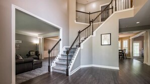 A spacious living area with a dark wood floor, a staircase with a black railing, and a dining area in the background. - NEW Southern Charm ATL 4 Bdr/3 Bath Executive Home (Norcross)
