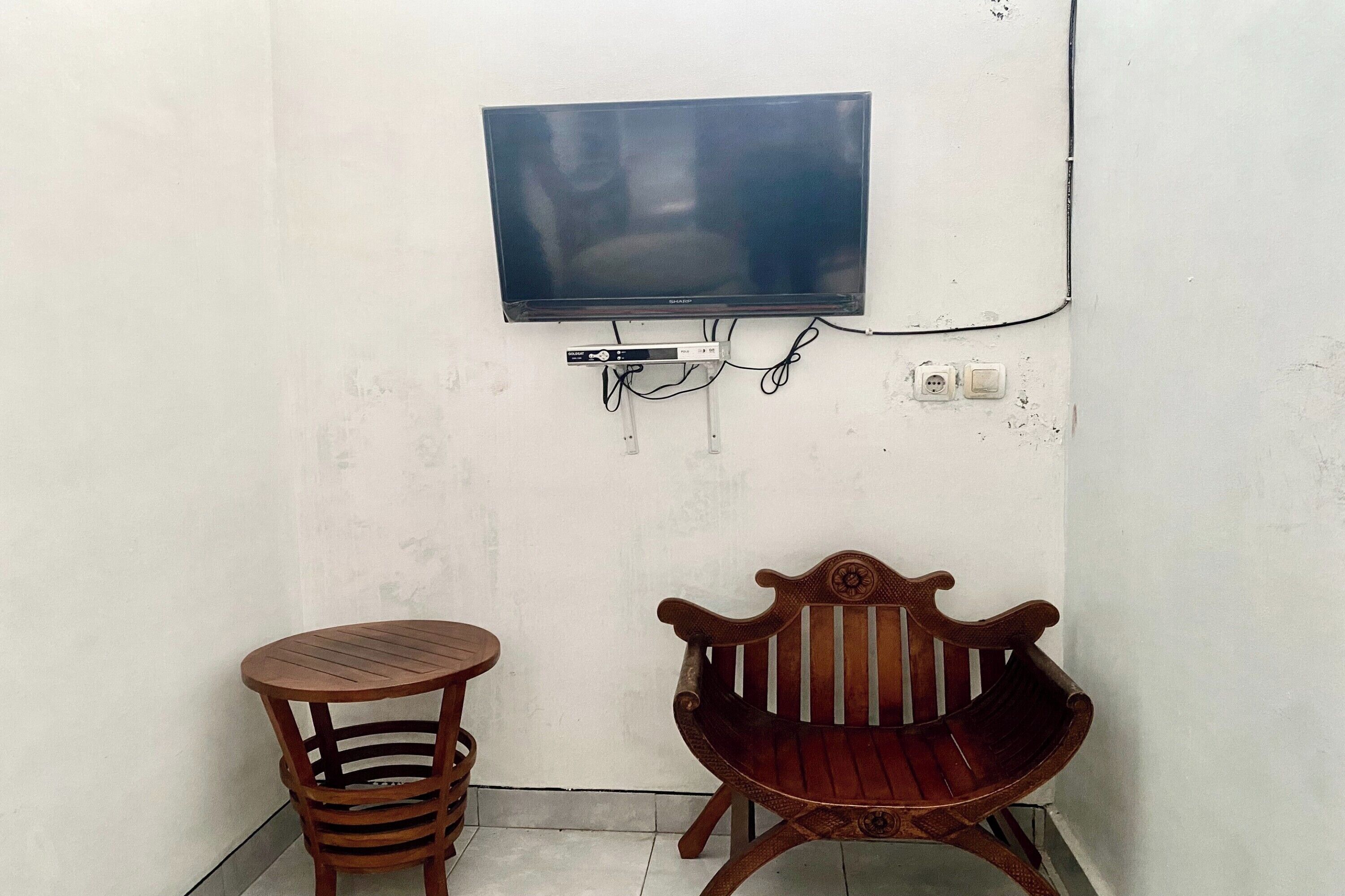 A small room with a flat-screen TV mounted on the wall, a wooden bench, and a round table.