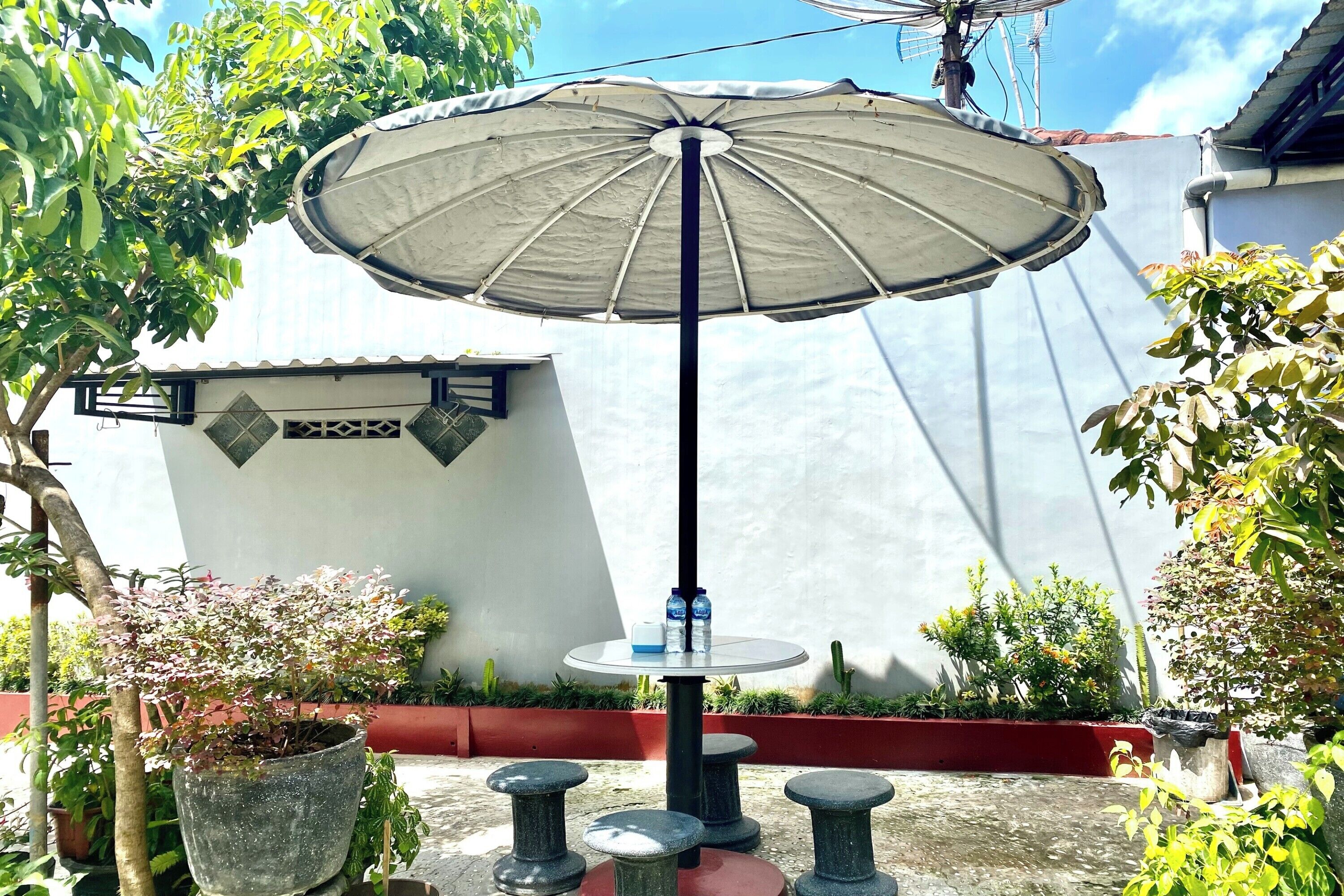 Un espace patio comprenant une table ronde, deux chaises, un grand parasol et des plantes en pot.