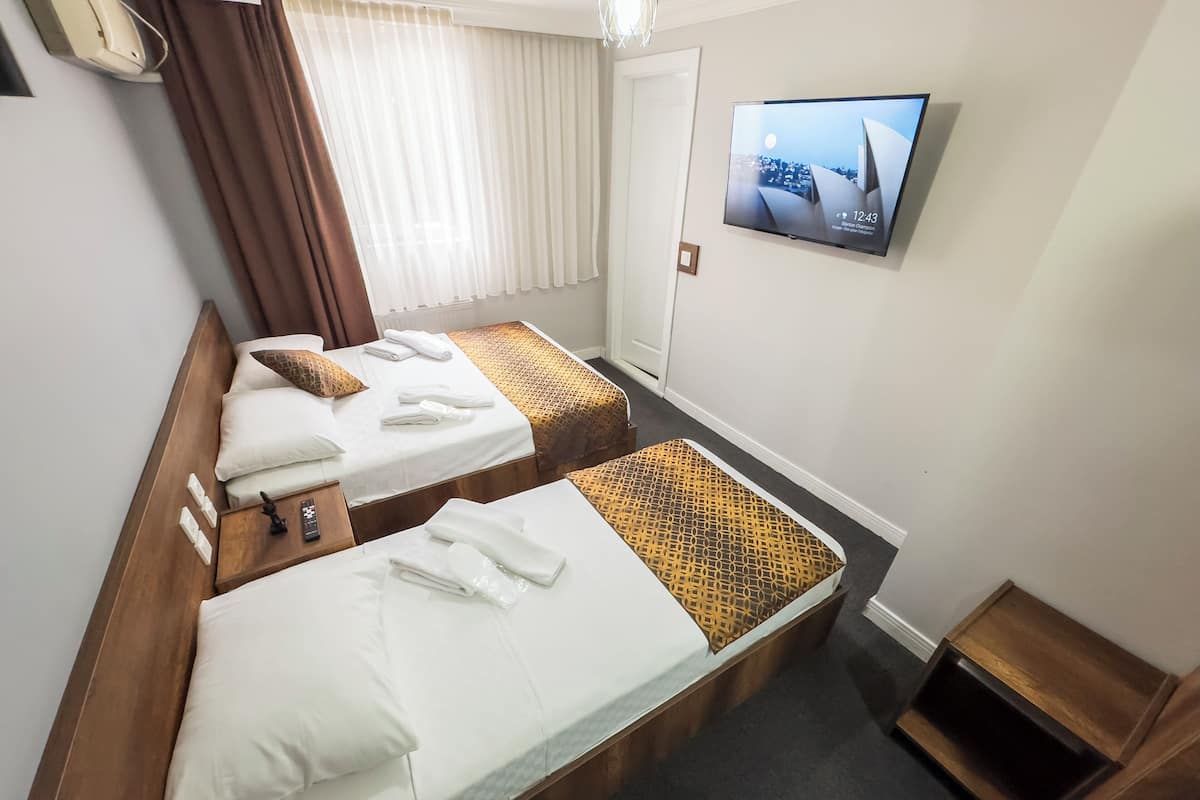 A hotel room with two beds, a TV on the wall, and a window with curtains.
