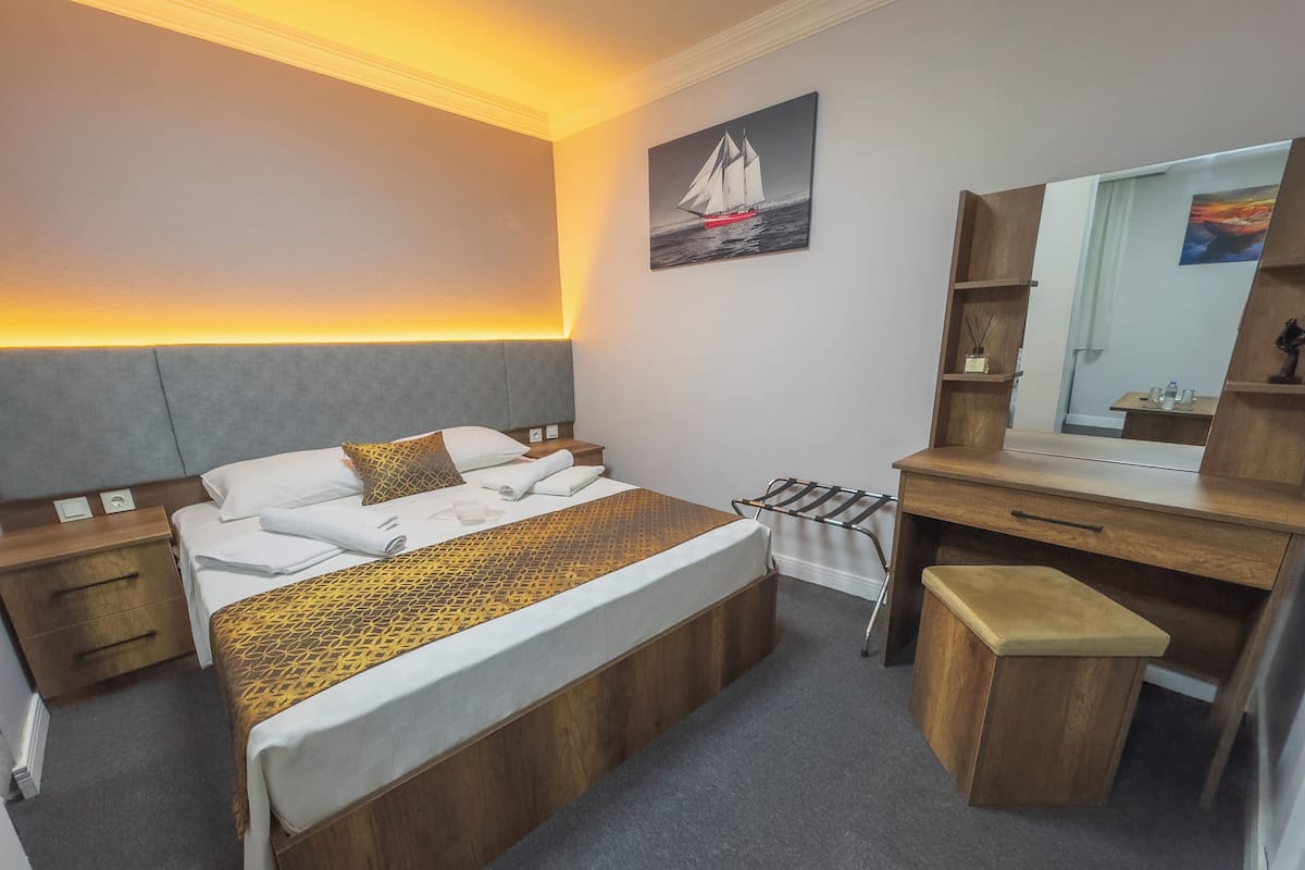 A hotel room with a bed, a desk, a chair, a mirror, and a towel rack.