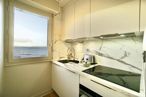 A compact kitchen with a view of the sea through a window, a sink, a stove, and a microwave.