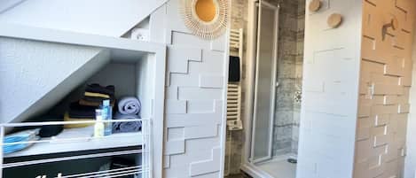 A compact bathroom with a shower, a towel rack, and a storage unit with folded towels.