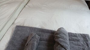 A neatly made bed with white linens and two pillows, a gray towel on the bed, and a wooden wall behind. - Urlaub im Schönen Calancatal (Augio)