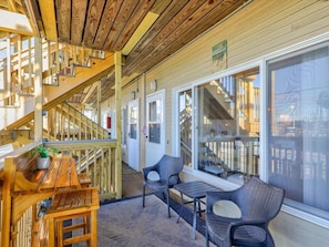 Step into a cozy outdoor space with a wooden staircase, bench, and wicker chairs, surrounded by a potted plant and a large window offering a view of the interior.
