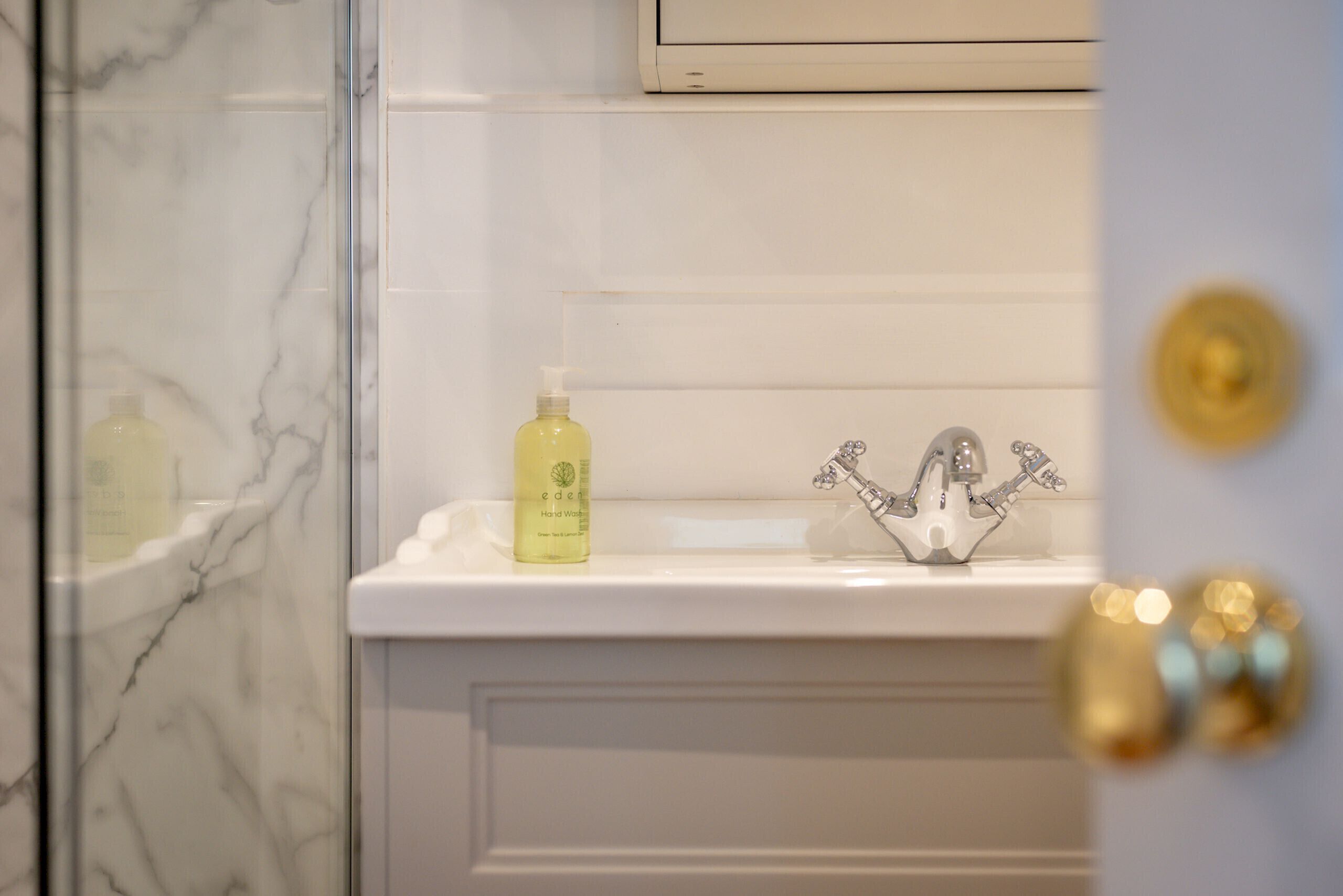 A bathroom with a marble wall, a white sink, a yellow bottle of hand soap, and a decorative faucet.