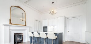 A modern kitchen with white cabinetry, a blue island with bar stools, a large mirror, and a chandelier.