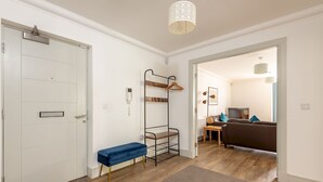 Un apartamento moderno con una puerta blanca, un banco, perchero y un comedor con sofá y mesa.