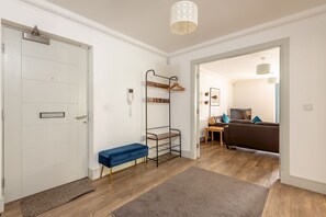 A modern apartment with a white door, a bench, a coat rack, and a dining area with a sofa and table.