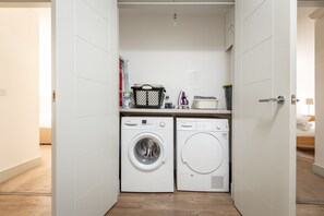 A compact laundry area with two front-loading washing machines, a drying machine, and a small countertop with various items. - Kingsbarns House (No 1) (St Andrews)