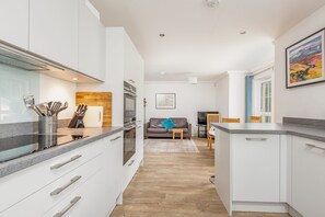 A modern kitchen with white cabinets, a granite countertop, and a wooden floor. - Kingsbarns House (No 1) (St Andrews)