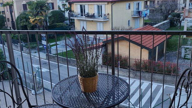 Un balcón con dos sillas y una mesa, con vista a una calle con edificios y montañas al fondo.