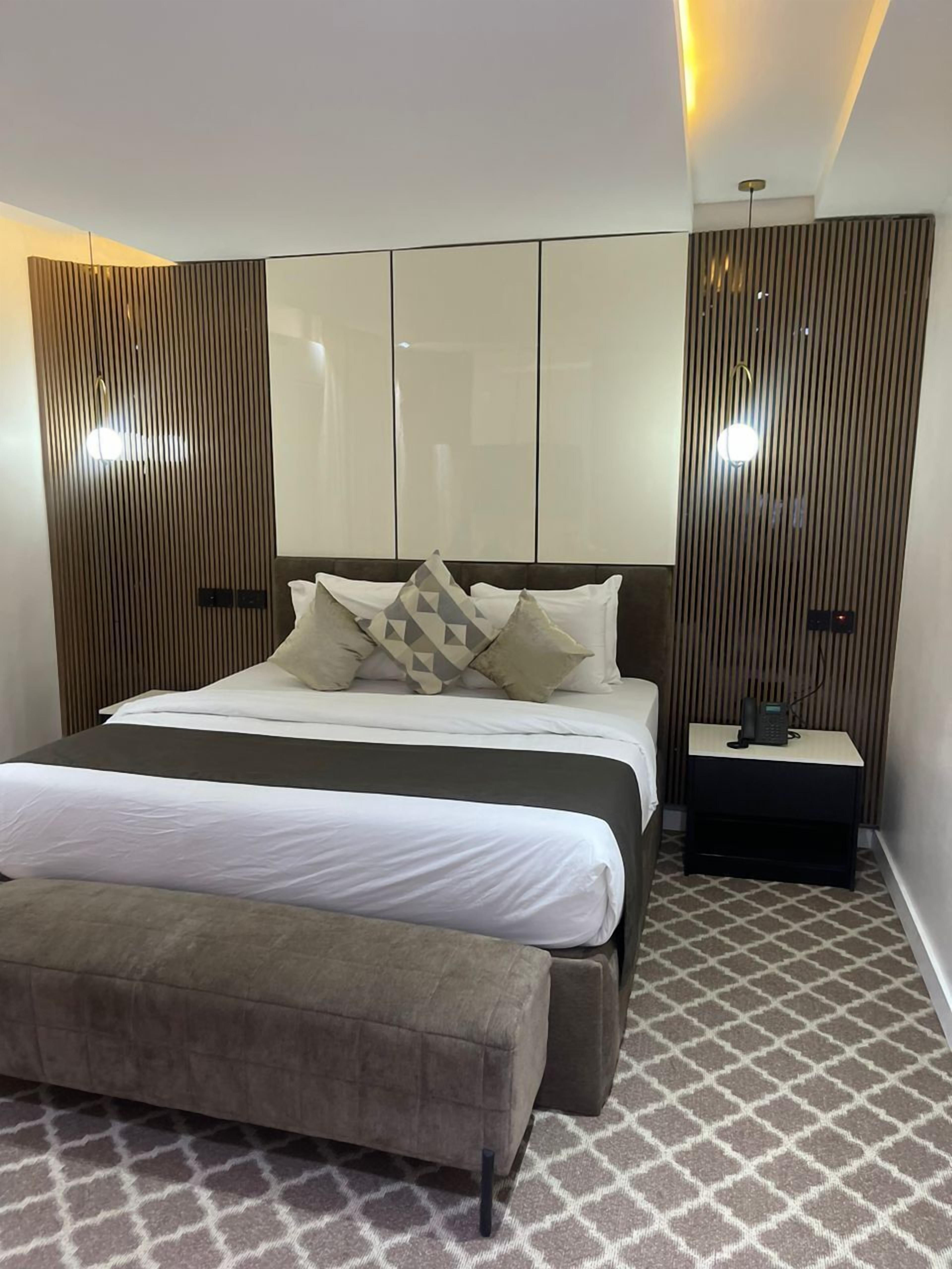 A modern bedroom with a large bed, a bedside table with a phone, and a patterned carpet.