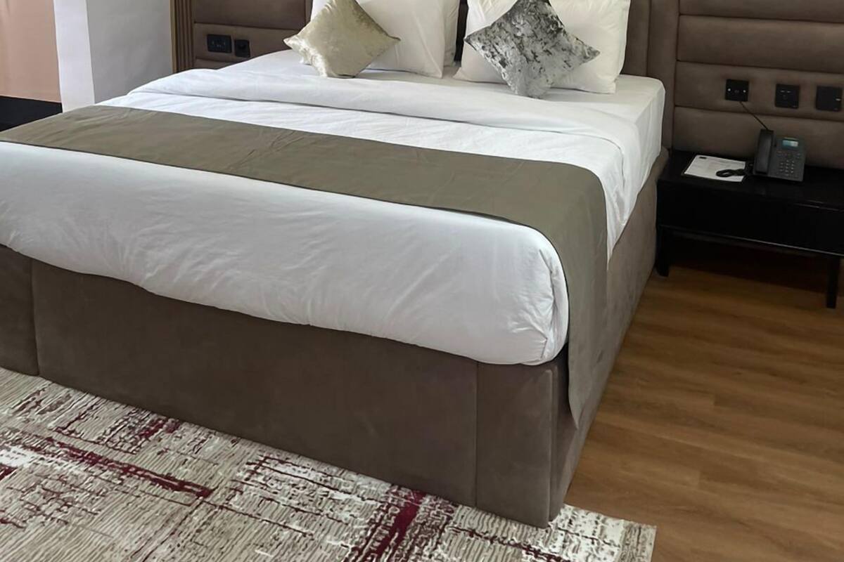 A modern bedroom with a large bed, a wooden headboard, and a bedside table with a phone and papers.