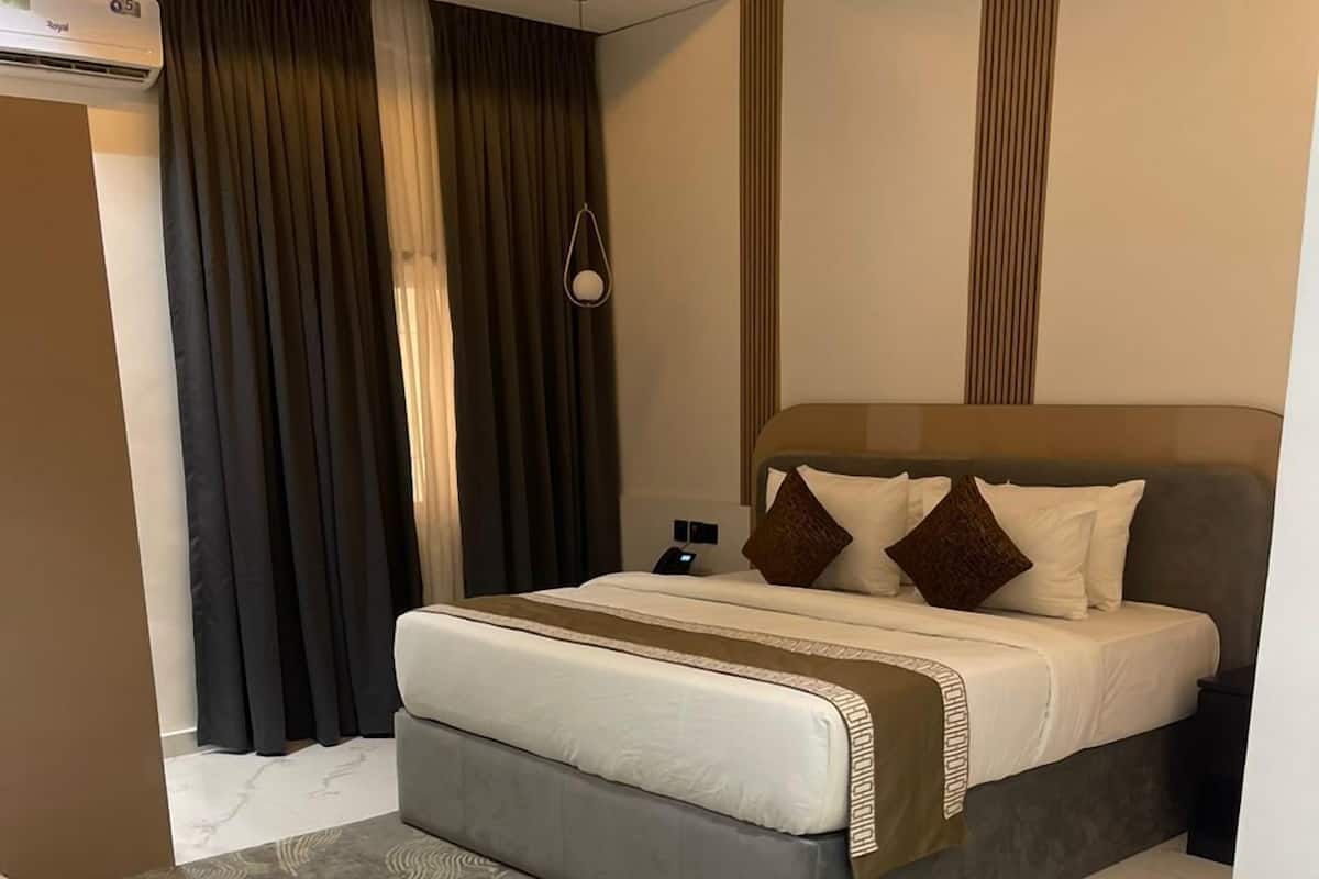 A modern bedroom with a large bed, a bedside table, a wall-mounted air conditioner, and a patterned rug.