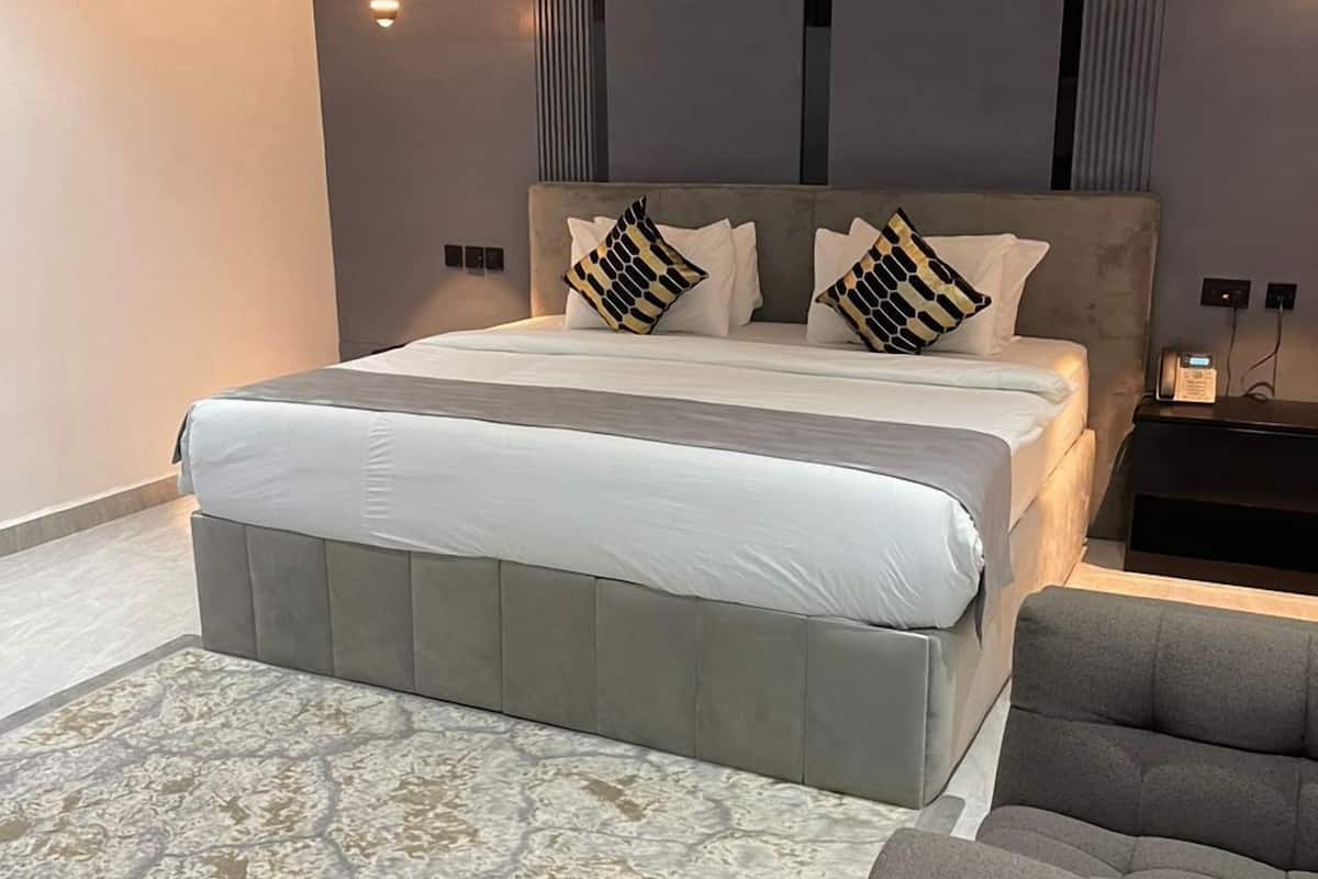 A modern bedroom with a large bed, a grey upholstered armchair, and a patterned rug.