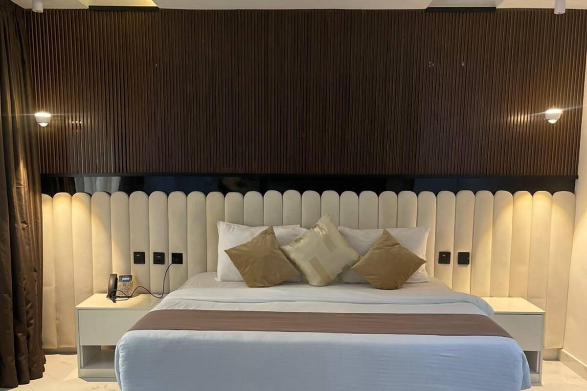 A modern bedroom with a large bed, a bedside table with a phone, and a wall-mounted light fixture.