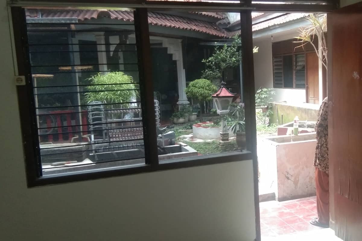 Ein Zimmer mit großem Fenster und Blick auf einen Innenhof mit Pflanzen und einem Gebäude im traditionellen Stil.