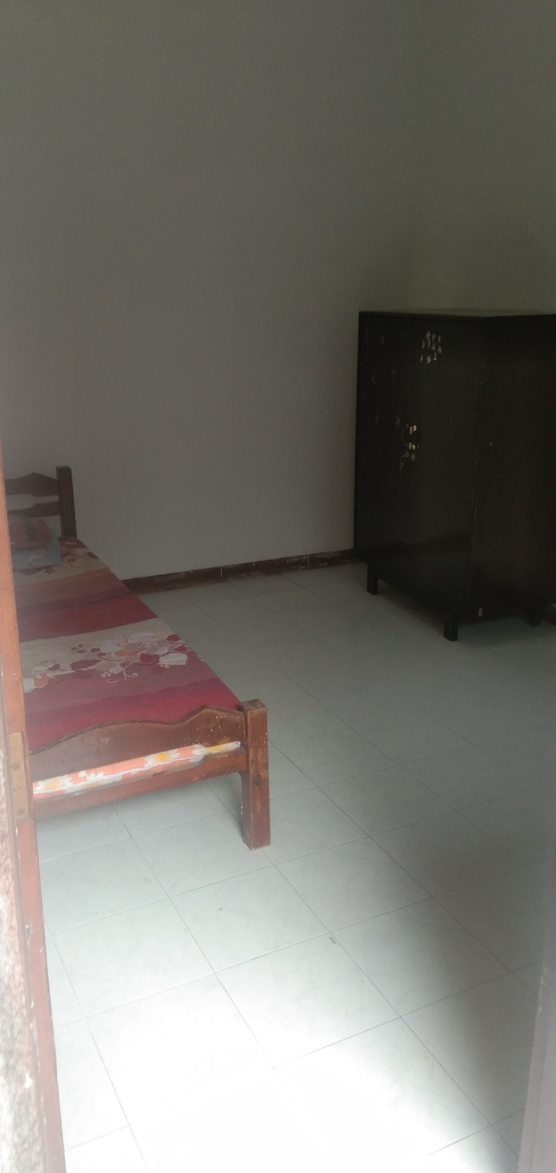 A room with a bed, a wooden cabinet, and a tiled floor.