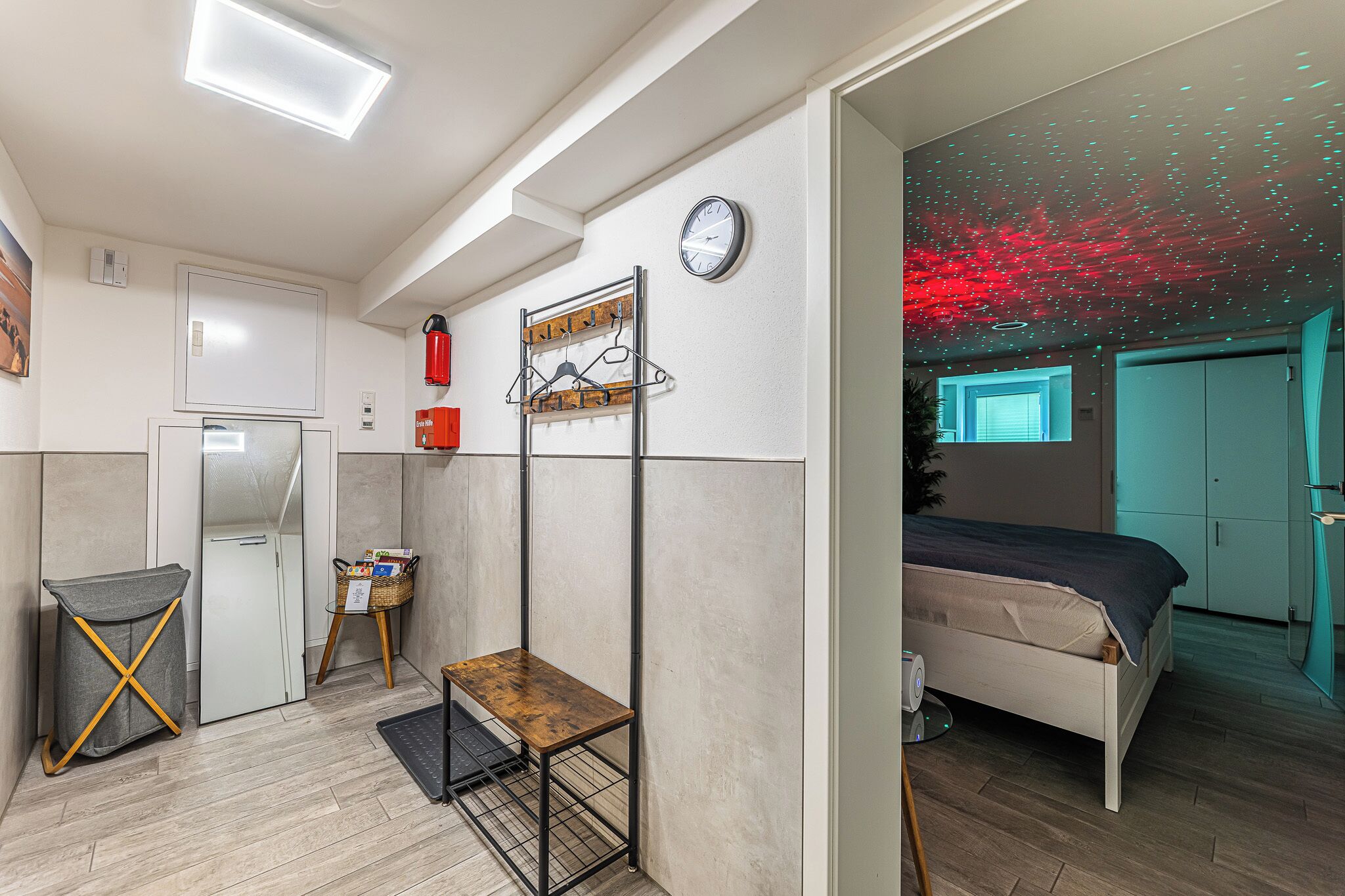 Ein modernes Zimmer mit einem Bett, einem kleinen Tisch, einer Wanduhr und einem Deckenprojektor.
