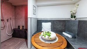 Een moderne badkamer met een houten wastafelmeubel, een ronde houten tafel met een taart, een handdoek en een potorkidee.