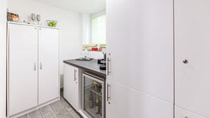 Een kleine keuken met witte kastjes, een inbouwkoelkast en een aanrecht met verschillende spullen.