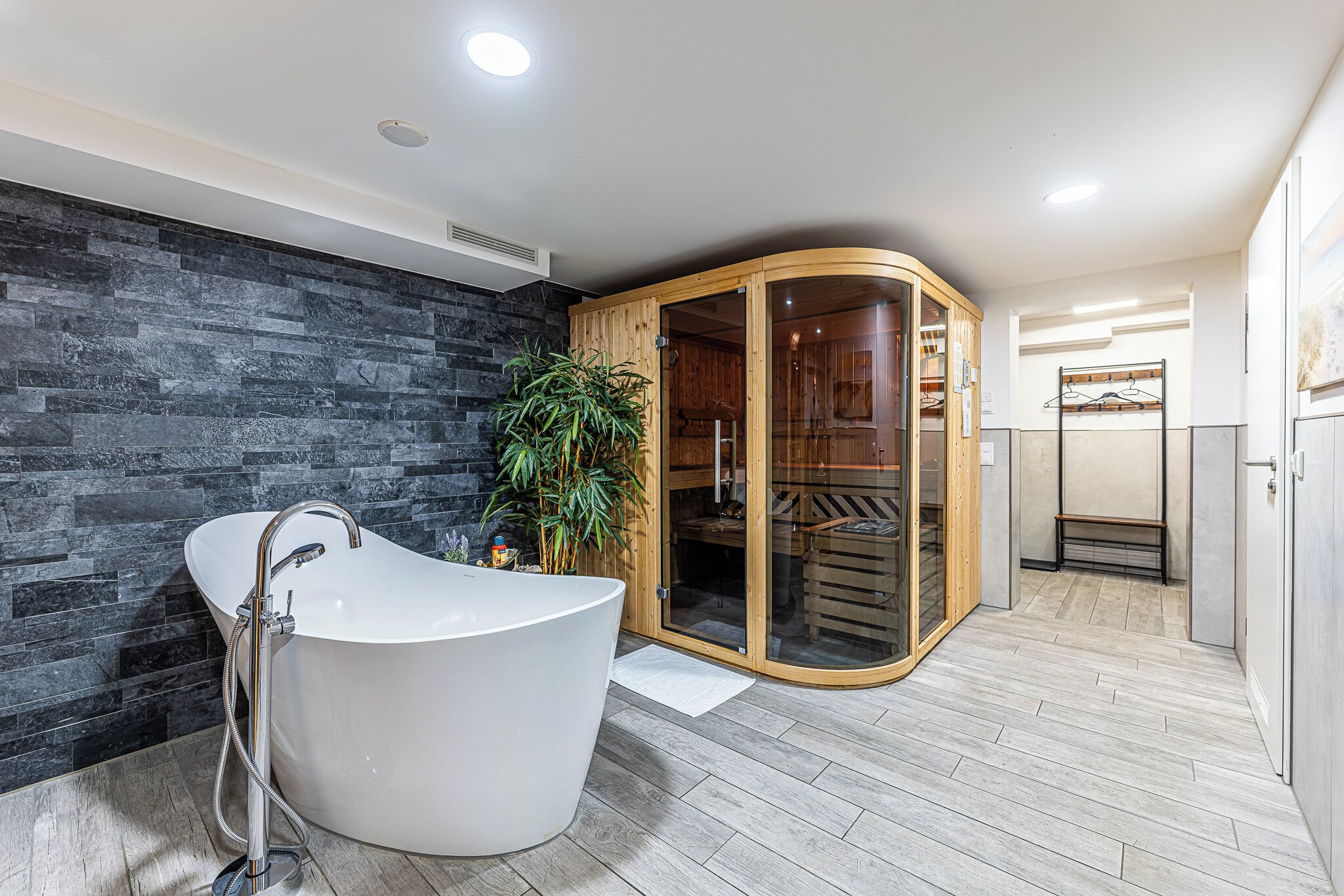 Ein modernes Badezimmer mit freistehender Badewanne, einer Holzsauna und einer Steinwand.