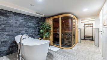 Ein modernes Badezimmer mit freistehender Badewanne, einer Holzsauna und einer Steinwand.